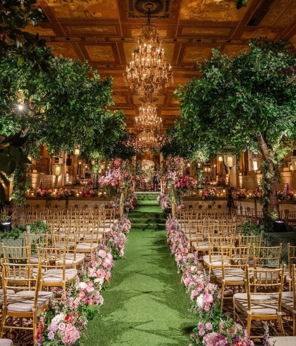 A lush indoor wedding aisle lined with gold chairs, blooming florals, and towering trees under grand chandeliers, creating a cinematic scene ideal for immersive ReLOOM VR event capture.