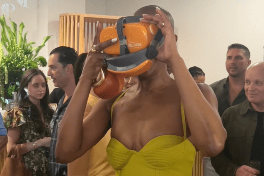 A woman in a green gown trying on an orange set of Reloom VR googles at an event.